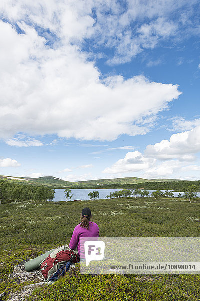 Sweden Harjedalen Ojon Woman with backpack sitting on rock and looking at lake