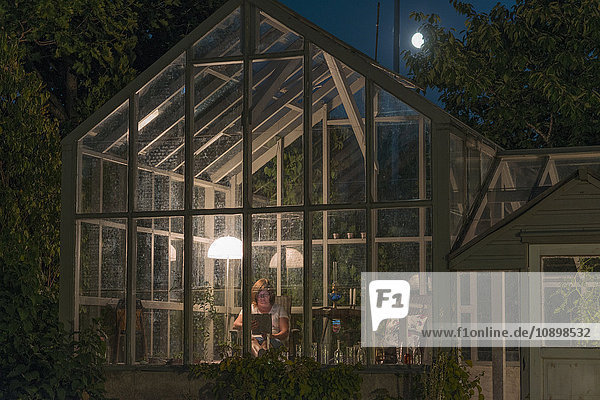 Schweden  Sodermanland  Stigtomta  Frau sitzend im Gewächshaus bei Nacht