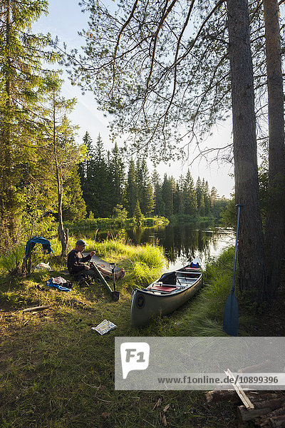 Schweden  Vastmanland  Svartalven  Mann im Kanu am Flussufer sitzend