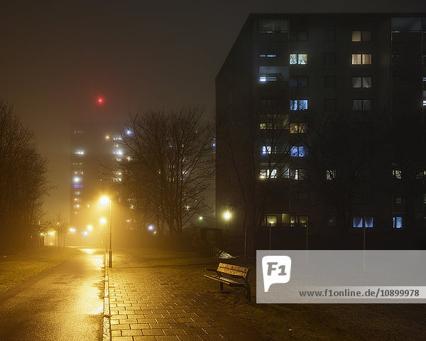 Schweden  Skane  Malmö  Rosengard  Beleuchtete Wohnhäuser entlang leerer Straße im Nebel
