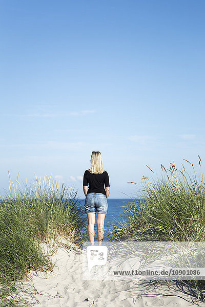 Schweden Skane Soderslatt Beddinge Rückansicht einer blonden Frau die am Strand steht und auf das Meer blickt.