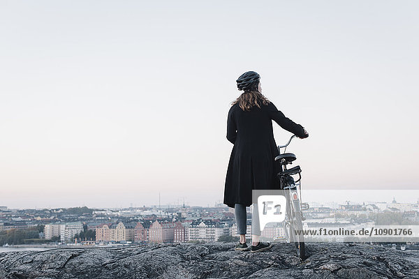 Schweden Sodermanland Stockholm Sodermalm Skinnarviksberget Rückansicht einer jungen Frau die mit dem Fahrrad auf dem Felsen steht.