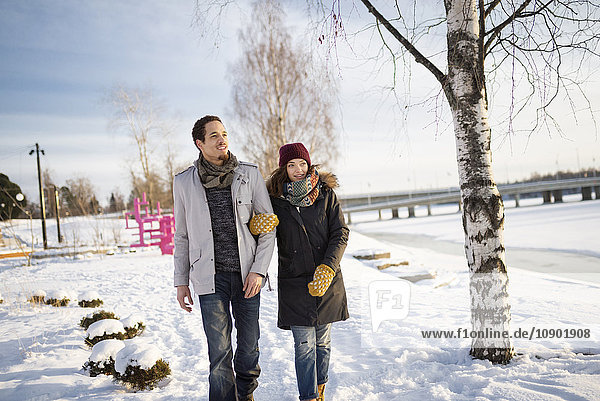 Schweden, Vasterbotten, Umea, Junges Paar beim Wandern im Schnee am Fluss