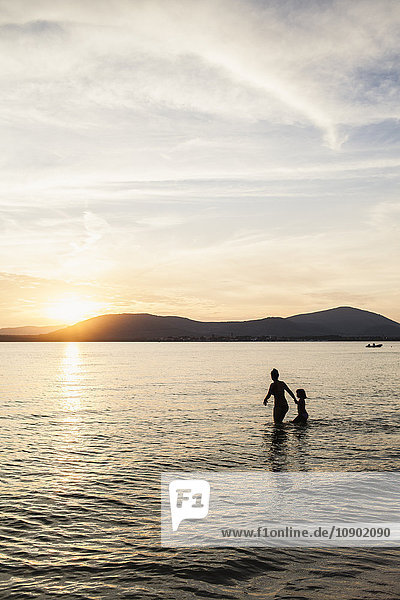 Italien Sardinien Alghero Mutter und Tochter waten im Meer bei Sonnenuntergang