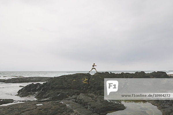 USA Hawaii Big Island Mann springt über eine Felsspalte am Meer