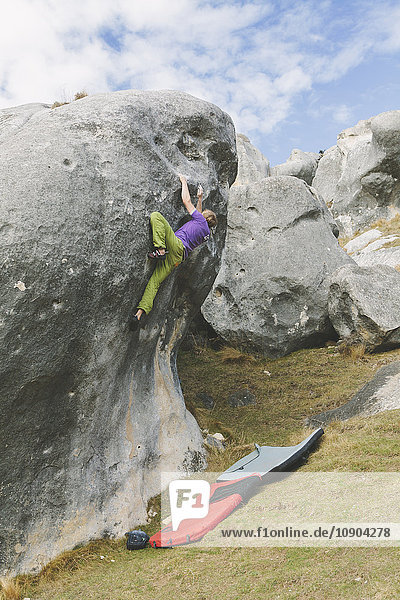 Neuseeland Castle Hill Junger Mann klettert auf Felsbrocken mit zwei Crashpads darunter