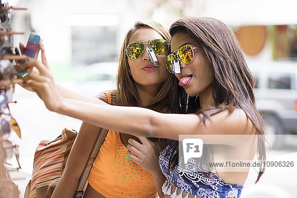 Two young women trying sunglasses on and taking a selfie