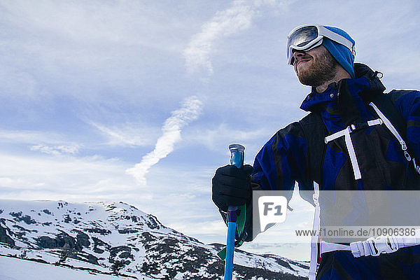 Man with ski goggles holding a ski pole in a snowy mountain landscape