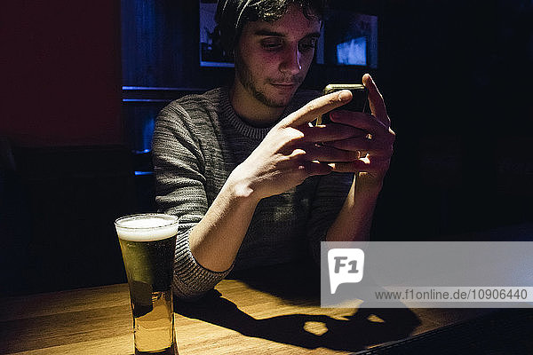 Man using his phone at a bar counter with a glass of beer