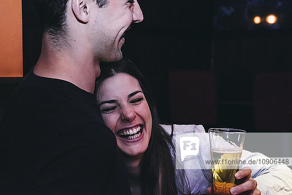 Laughing woman leaning on the chest of a man drinking beer in a bar