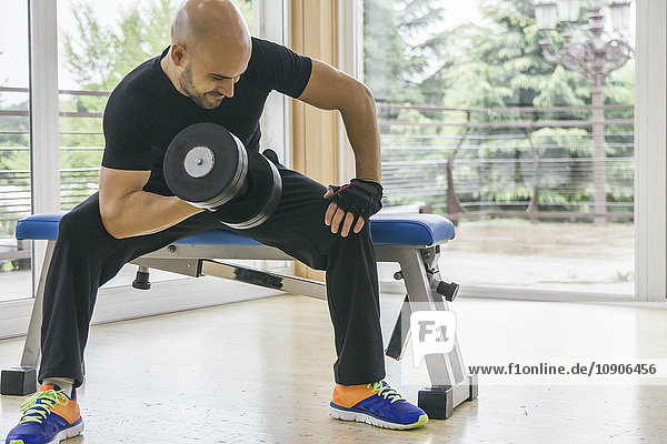 Man lifting a dumbbell sitting on a bench in a gym