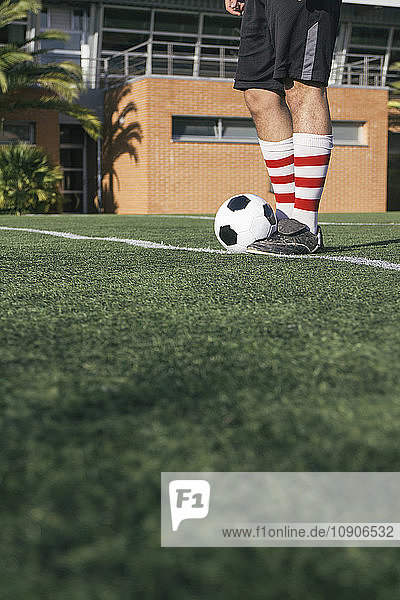 Legs of football player with ball on football ground