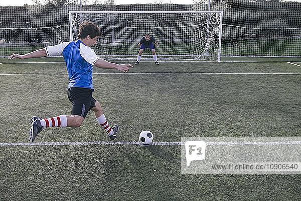 Football player kicking a ball in front of a goal with a goalkeeper