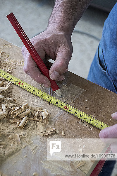 Hands of a carpenter measuring a wood plank with a tape measure and pencil