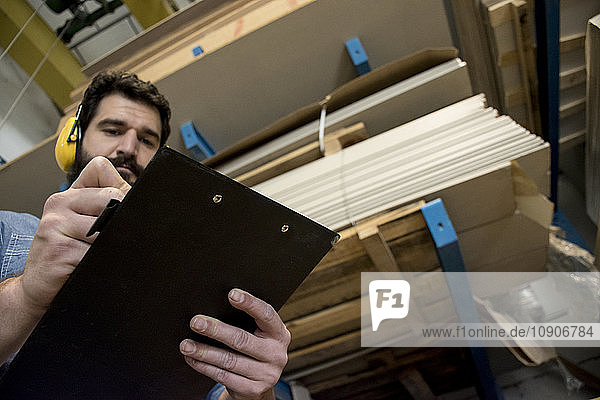 Man with hearing protection making notes in a folder in a warehouse of a factory