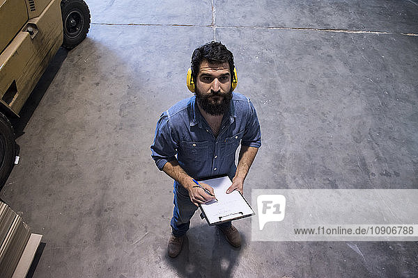 Man with hearing protection making notes in a folder in a warehouse of a factory