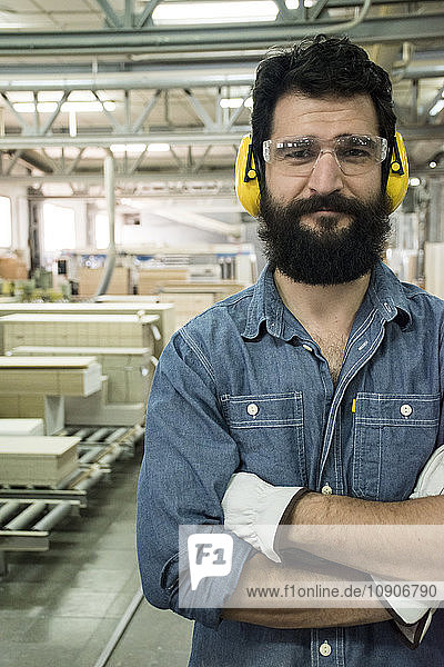 Man with hearing protection  safety glasses and gloves smiling with his arms crossed in a factory