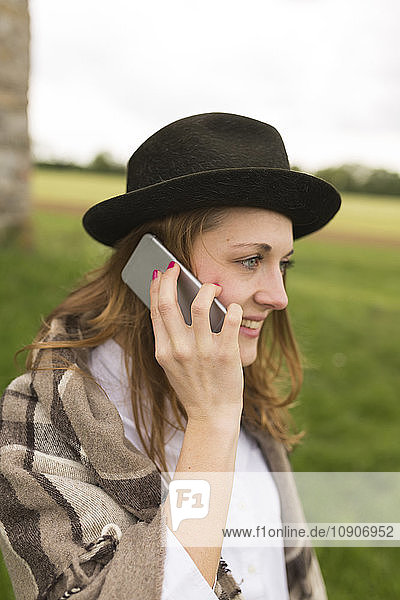 Young woman wearing hat telephoning with smartphone at countryside