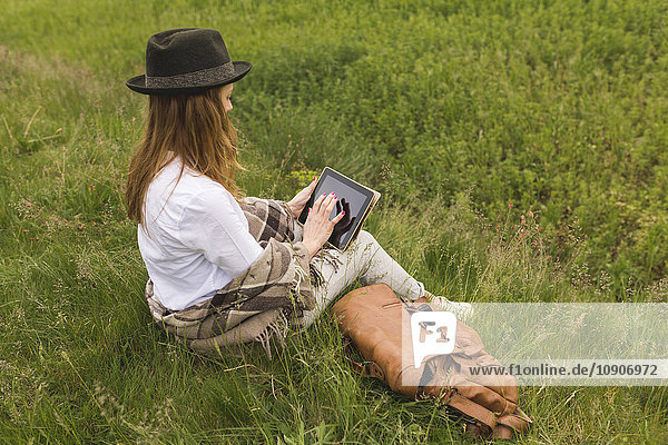 Woman sitting on a meadow using digital tablet