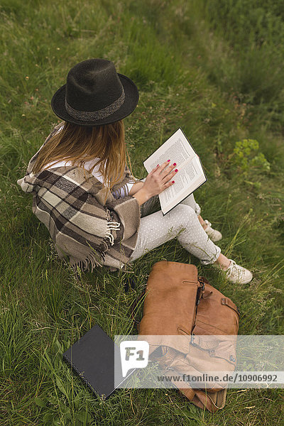 Young woman sitting on a meadow reading a book