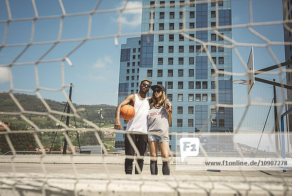 Junges Paar steht auf dem Basketballfeld und schaut in die Kamera.