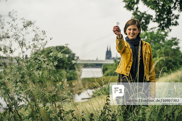 Deutschland  Köln  glückliche Frau stehend auf einer Wiese mit einer Pflanze