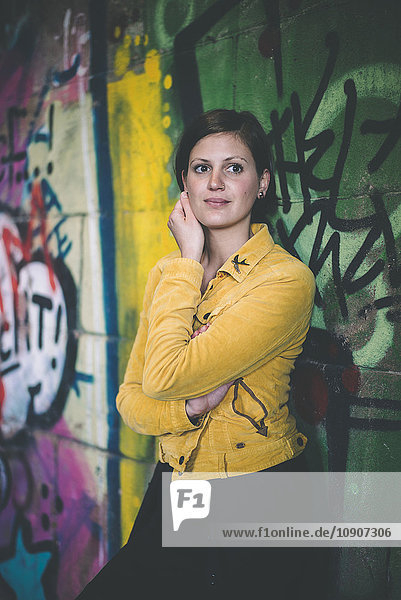 Porträt einer jungen Frau in gelber Jacke vor Graffiti stehend