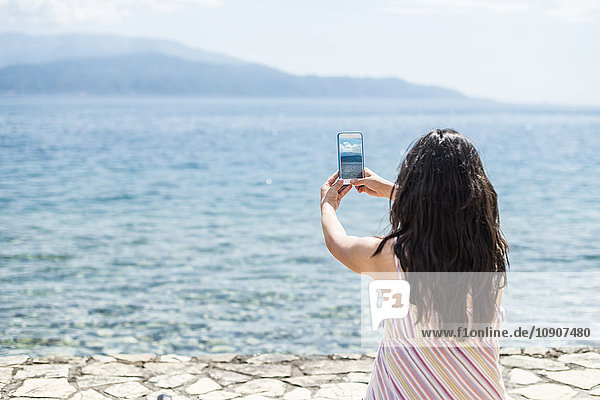Griechenland  Sergoulas  Frau beim Fotografieren mit dem Smartphone an der Küste