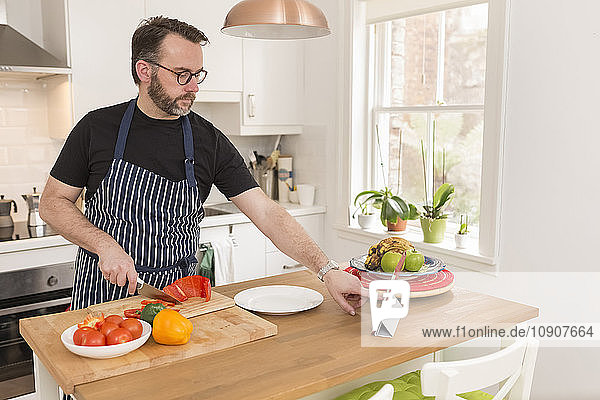 Man using digital tablet in his kitchen while preparing vegetables