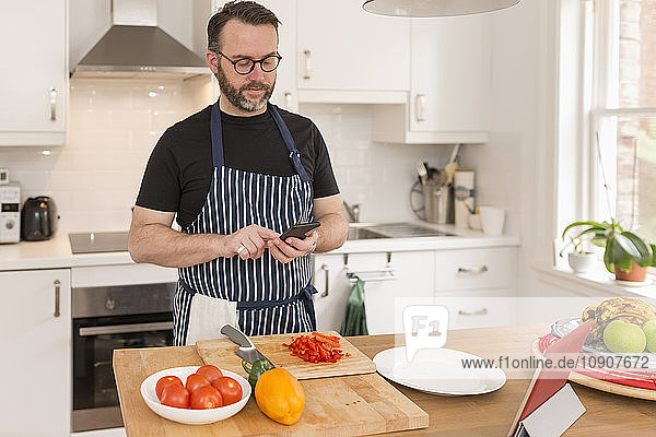 Portrait of man using smartphone while preparing food in the kitchen