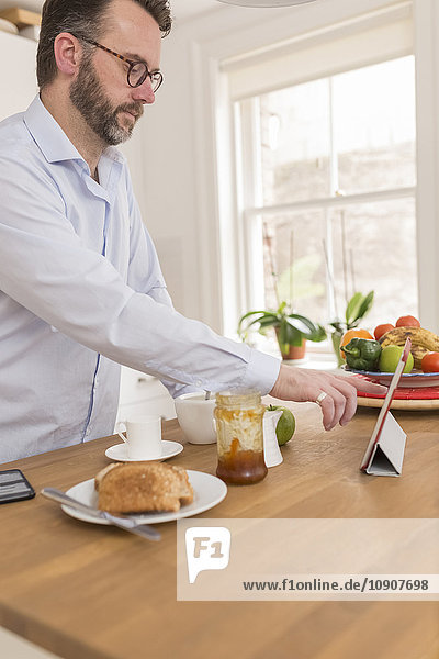 Mann steht am Frühstückstisch in der Küche mit digitalem Tablett