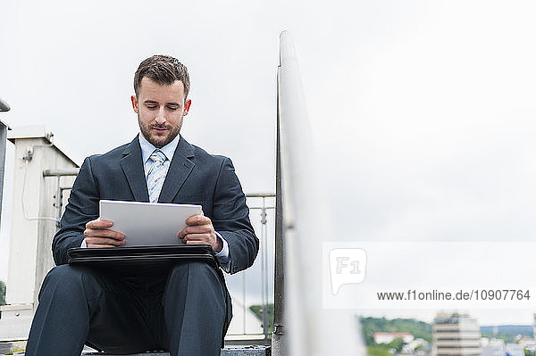 Businessman sitting on stairs looking at digital tablet