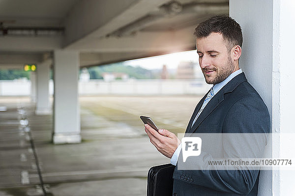 Businessman looking at cell phone in parking garage