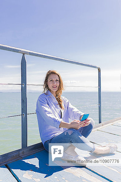 Italy  Lignano Sabbiadoro  woman sitting with smartphone on jetty
