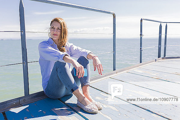 Italy  Lignano Sabbiadoro  woman sitting with smartphone on jetty