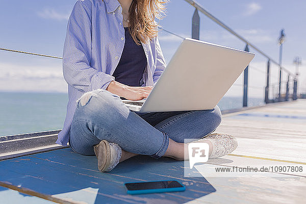 Young woman with laptop and smartphone  sitting on jetty