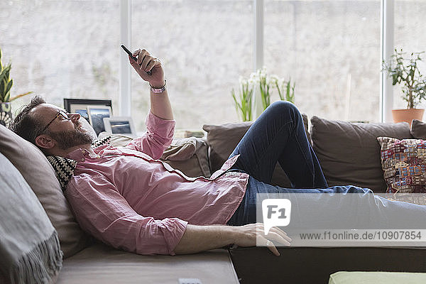 Mature man lying on couch taking selfie