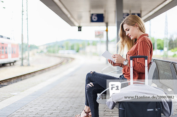 Young woman sitting on bench at platform using tablet