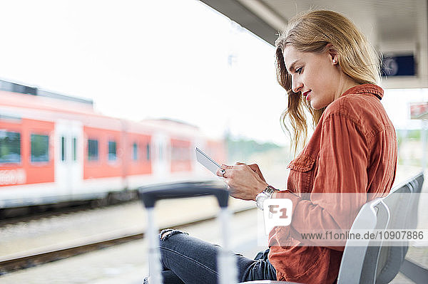 Young woman sitting on bench at platform using tablet