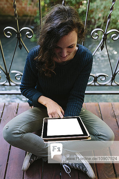 Young woman sitting on balcony working with digital tablet