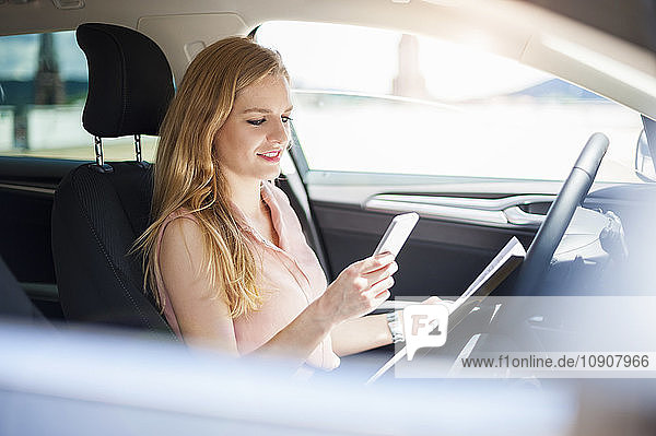 Young businesswoman sitting in her car looking at cell phone
