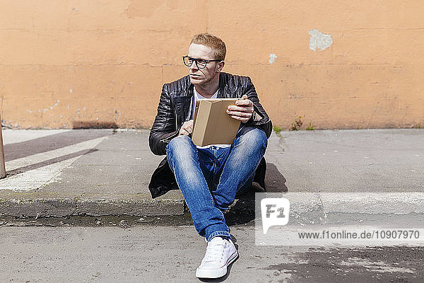 Young man with digital tablet sitting at curb