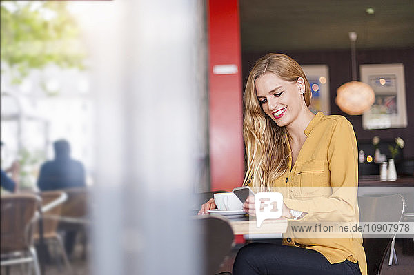 Smiling young woman sitting in a coffee shop looking at smartphone