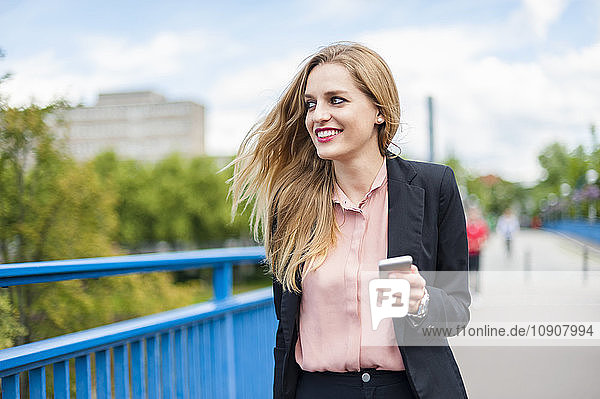 Smiling businesswoman on a bridge with smartphone