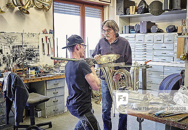 Two instrument makers repairing brass instrument in workshop