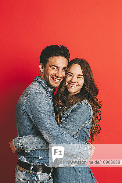 Portrait of happy young couple hugging each other in front of red background