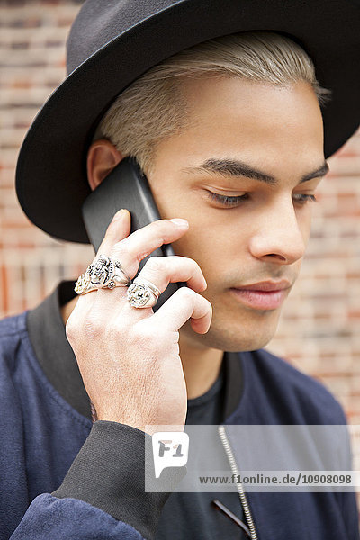 Portrait eines jungen Mannes mit Ringen und Huttelefonie mit Smartphone