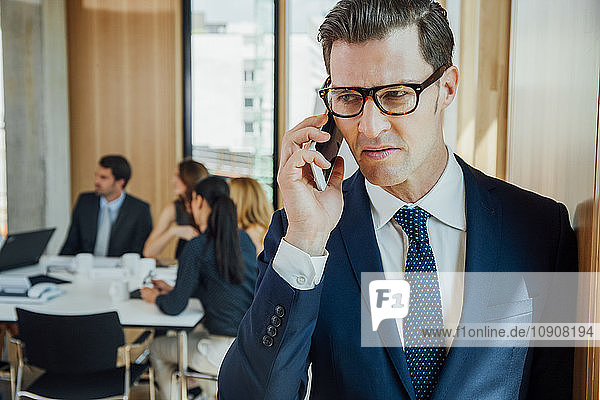 Businessman on the phone with meeting in background