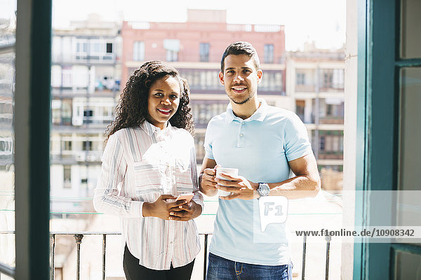 Two young business people standing on balcony with cup of coffee