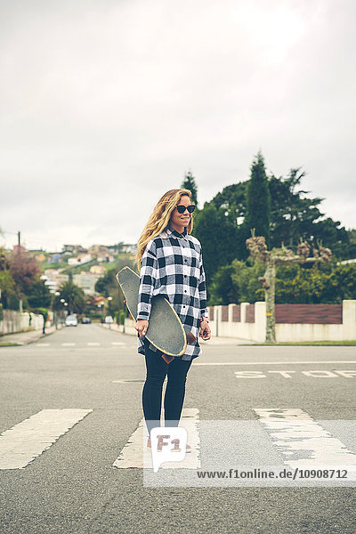 Lächelnde junge Frau mit Skateboard auf der Straße
